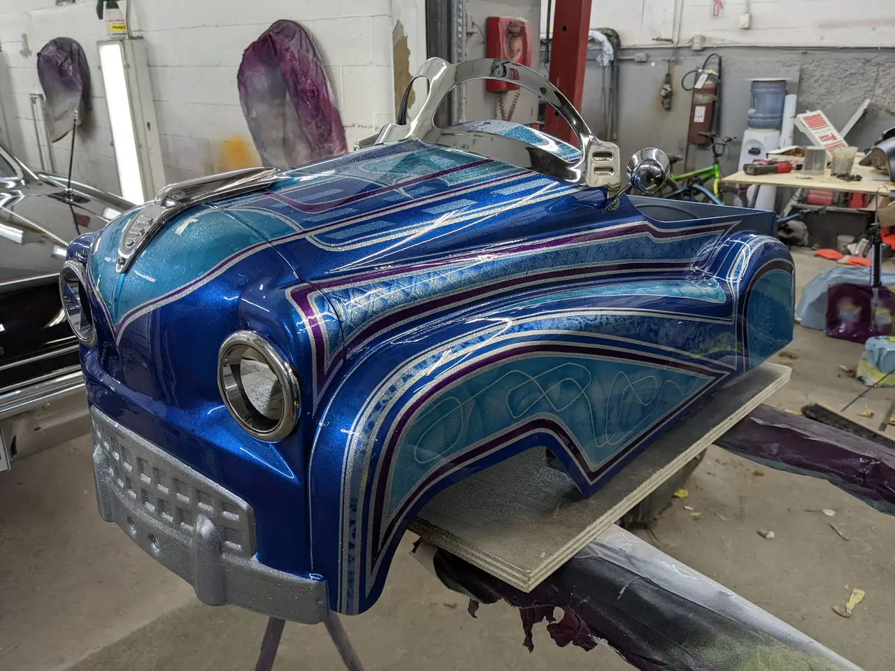 Carrosserie personnalisée bleue à paillettes avec filets et effets de dentelle, sur support d’atelier